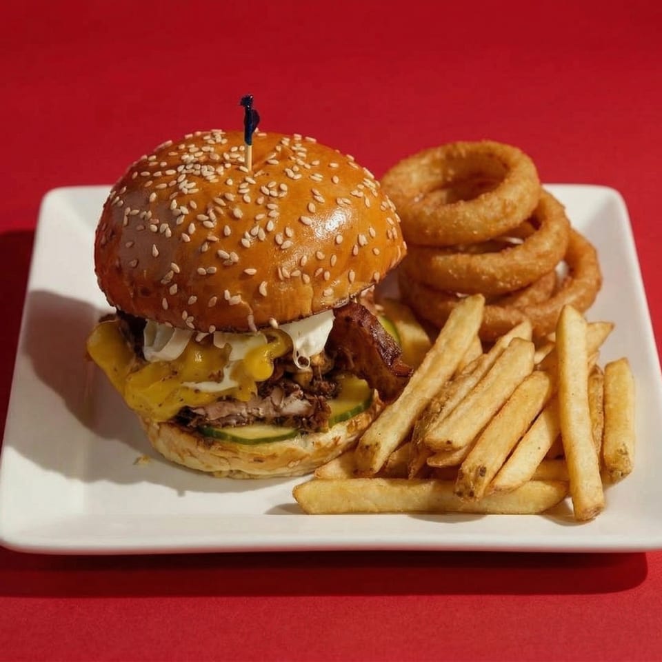 A loaded burger with melted cheese, pickles, and bacon, served with fries and onion rings.