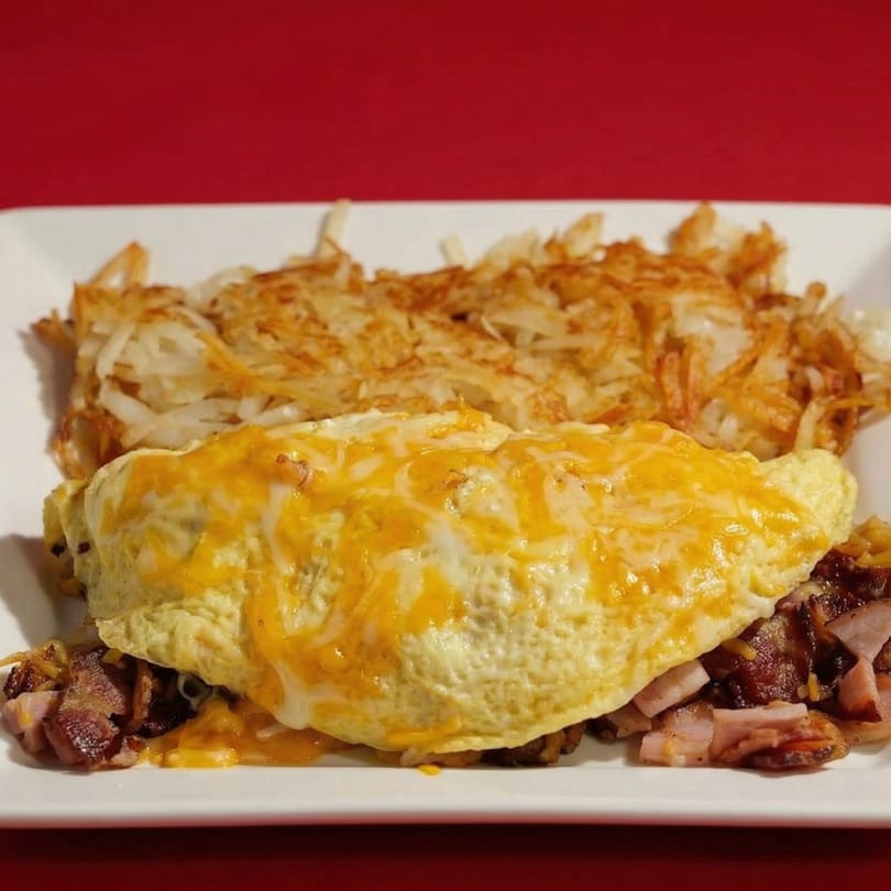 A cheesy omelet with bacon and ham, served with hash browns on a white plate.