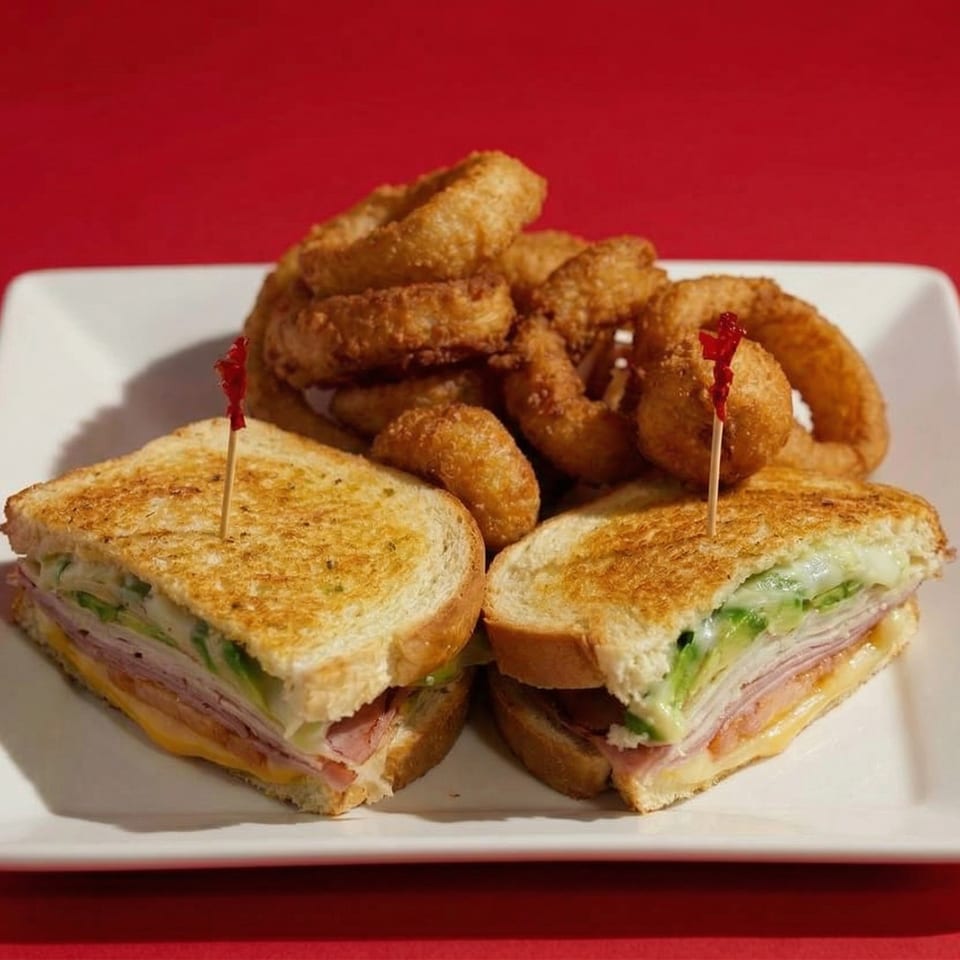 Grilled sandwiches with ham, cheese, and avocado, served with a side of crispy onion rings.